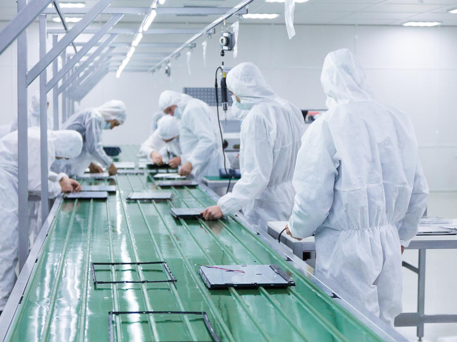 Workers in clean-room suits and masks carefully assemble laptops at a precision assembly line, ensuring a high-quality manufacturing process.