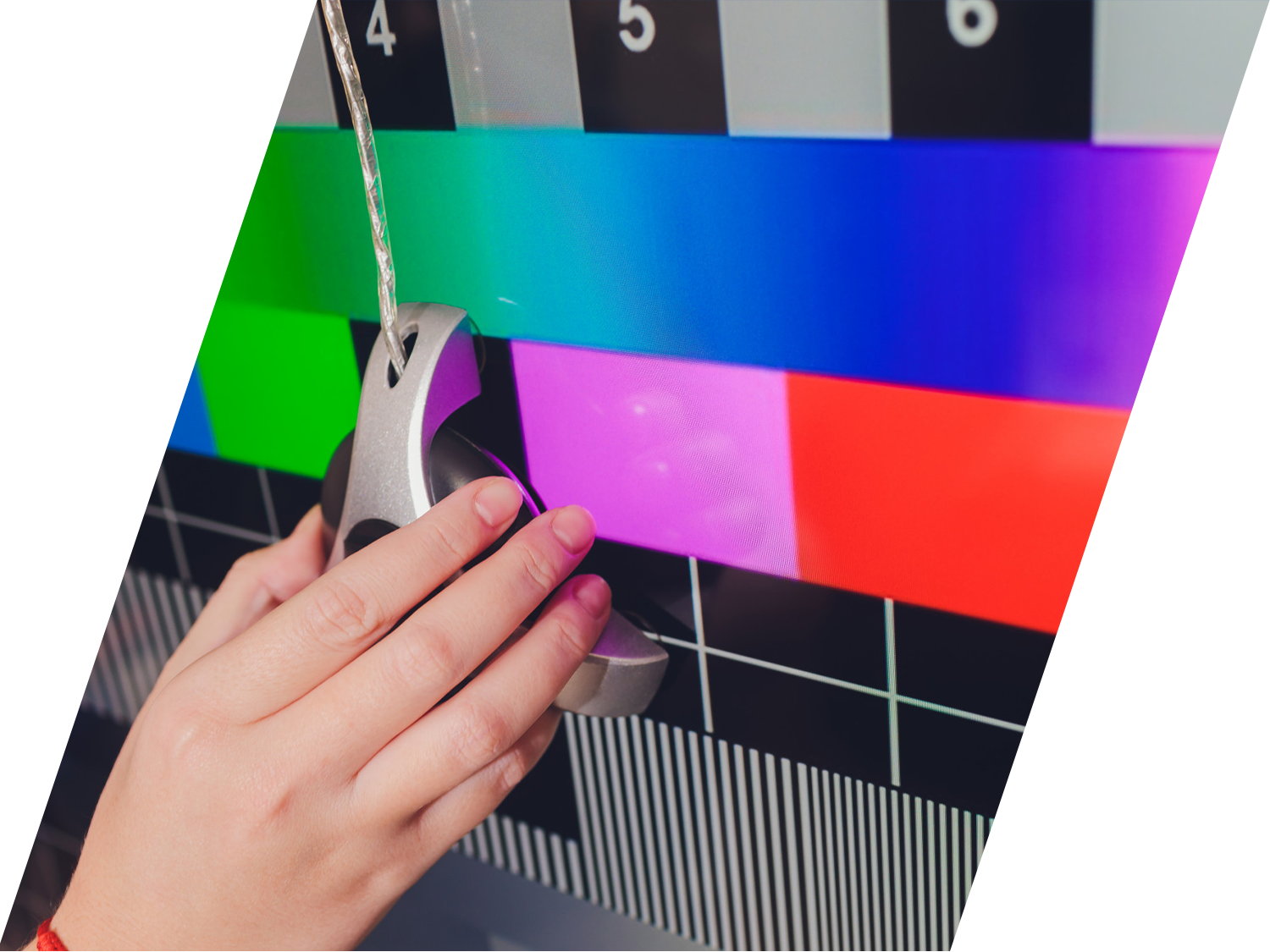 A hand holds a colorimeter calibration tool against a computer monitor displaying a bright multicolor test pattern to ensure high quality color accuracy.