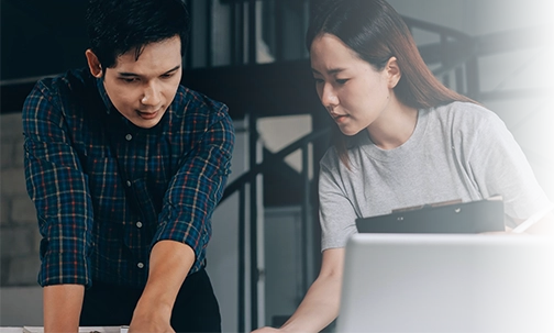 A male and female professional collaborating over a laptop screen and analyzing project details together.