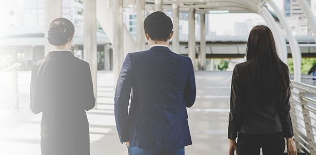 Rear view of three business professionals in formal attire walking together through an urban commercial area.